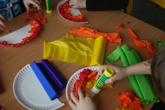 na stole połówki papierowych talerzyków i kolorowa bibuła, na talerzykach kulki z bibuły