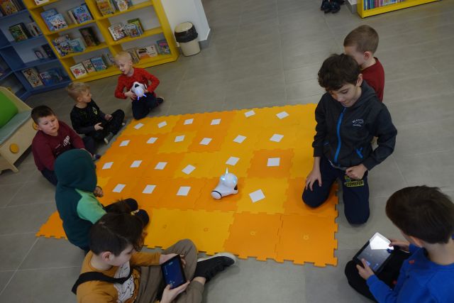 dzieci sterują przy pomocy tabletów robotami na pomarańczowych puzlach