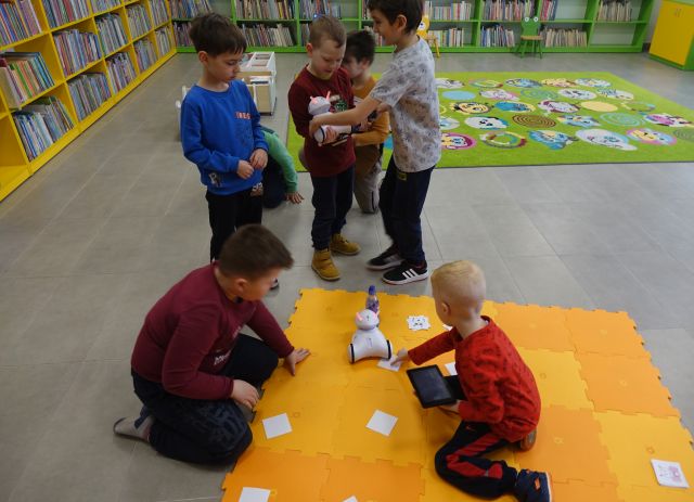 dzieci sterują przy pomocy tabletów robotami na pomarańczowych puzlach