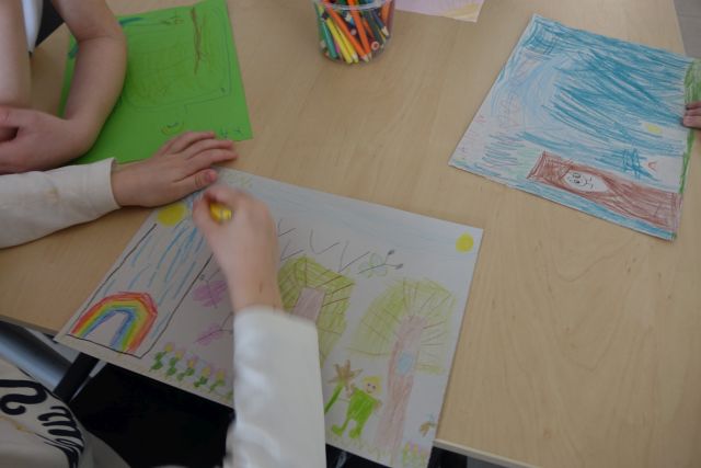 kartki z rysunkami na stoliku i dłonie dzieci rysujące