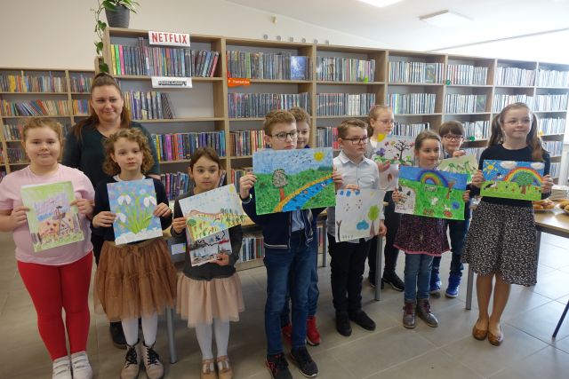 dzieci nagrodzone w konkursie pozują do zdjęcia z pracami plastycznymi przez siebie wykonanymi na tle regałów z książkami