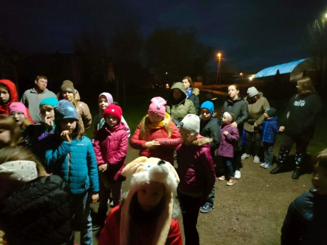 uczestnicy spotkania dzieci i dorośli w ciemności ubrani stoją w parku