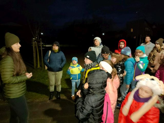 uczestnicy spotkania dzieci i dorośli w ciemności ubrani stoją w parku