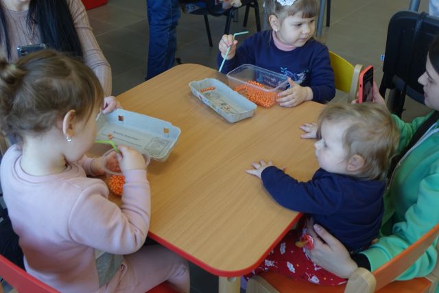 dzieci siedzą przy stołach i mieszają w koralikach