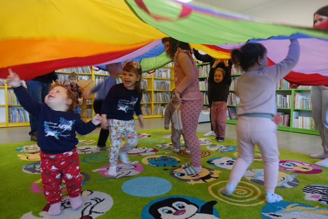 rodzice trzymają kolorową chustę, pod nią radosne dzieci