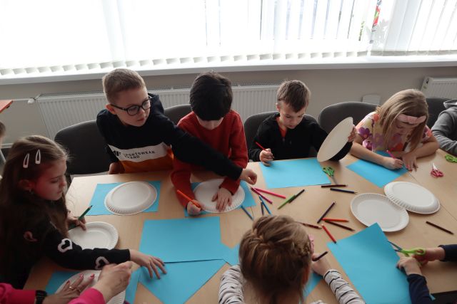 dzieci przy stołach wyklejają na niebieskich kartkach kwiaty