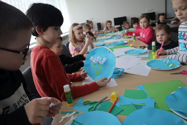 dzieci wyklejają na papierowych talerzykach oklejonych niebieską kartką kwiaty
