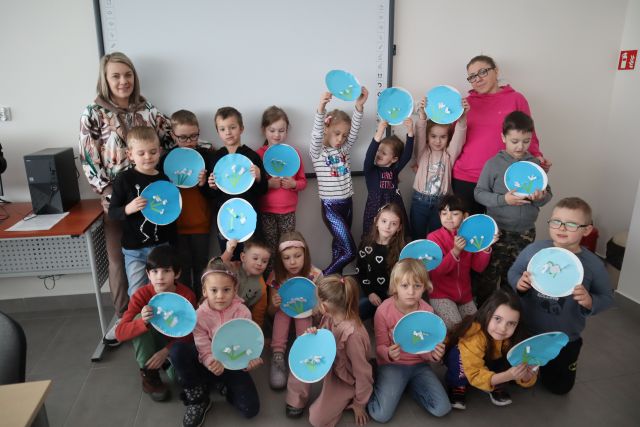 dzieci pozują do zdjęcia z wykonanymi przez siebie kwiatami przyklejonymi do papierowych talerzyków oklejonych niebieskim papierem