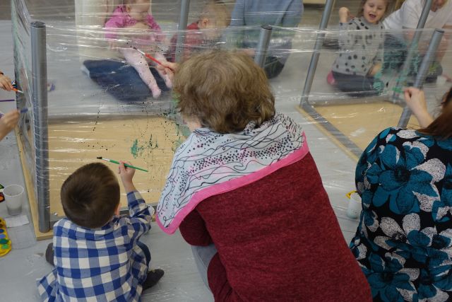 dzieci i rodzice malują farbkami po folii przymocowanej do stolików