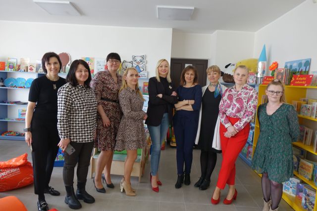 7 kobiet pozuje do zdjęcia, w tle kolorowe regały