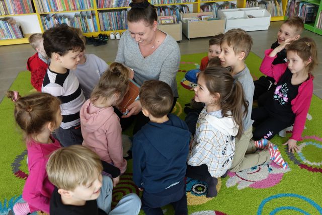 dzieci siedzą przy kobiecie i wąchają pachnącą książkę