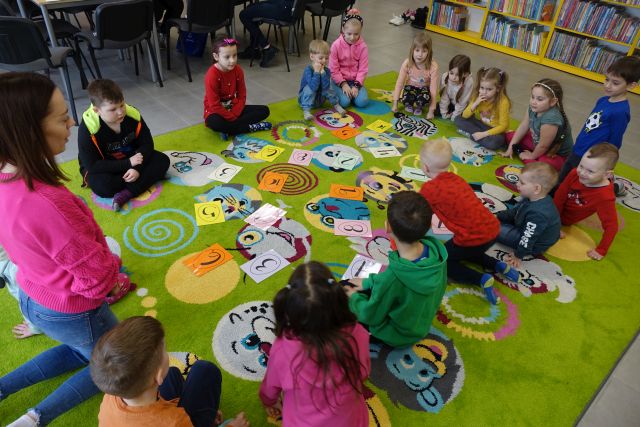 dzieci siedzą na zielonym dywanie, przed nimi leżą kartki z liczbami