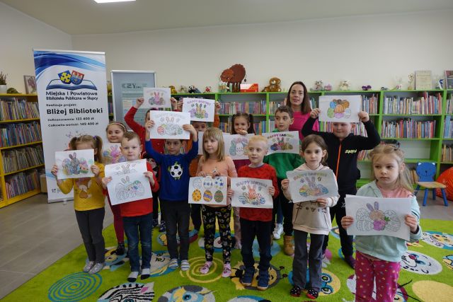 dzieci i kobieta pozują do zdjęcia z wykonanymi przez siebie rysunkami na kartkach