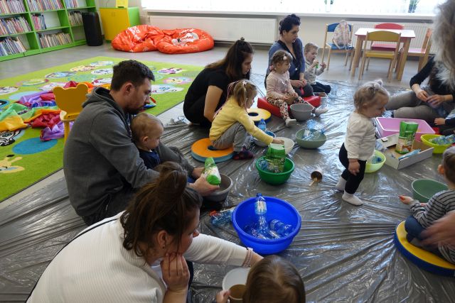 dzieci i rodzice siedzą na podłodze i robią z balonów i mąki gniotki