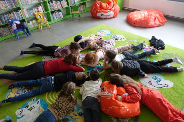 9 dzieci i kobieta leżą na brzuchach na kolorowym dywanie