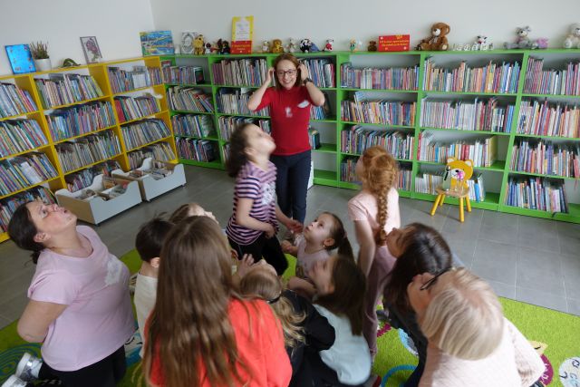 dzieci i kobieta na dywanie dmuchają w piórka