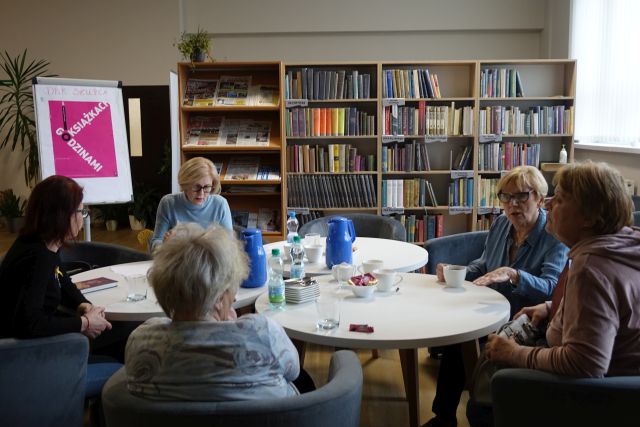6 kobiet siedzi przy białych okrągłych stołach, w tle regały z książkami