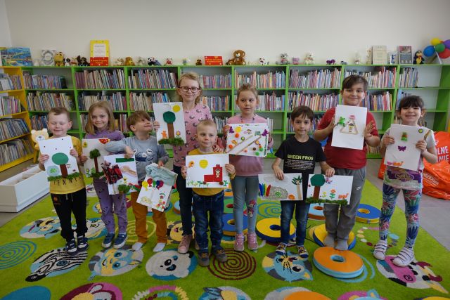 uczestnicy warsztatów pozują do zdjęcia z wykonanymi przez siebie książkami dotykowymi, w tle regały z książkami