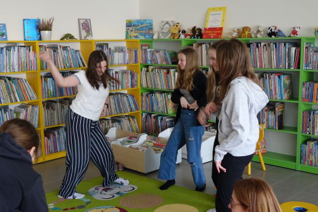 dziewczyny tańczą na kolorowym dywanie, w tle regały z książkami