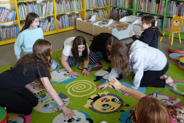 dziewczyny siedzą pochylone na mkolorowym dywanie