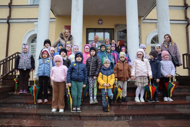 przedszkolaki pozują do zdjęcia ze starostą na schodach przed starostwem powiatowym, mają przypięte żółte żonkile z papieru
