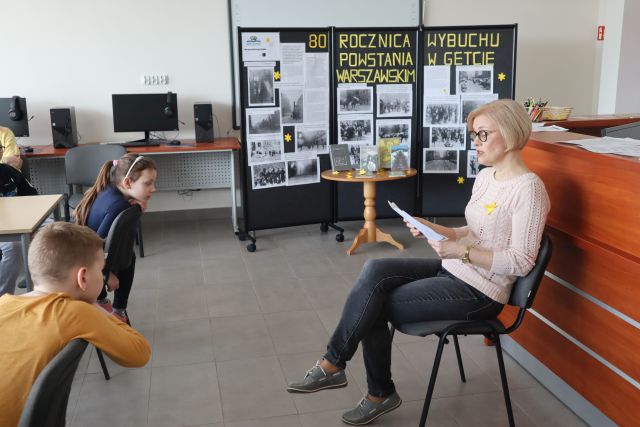 kobieta czyta dzieciom, w tle wystawa na temat 80 rocznicy wybuchu powstania w getcie warszawskim