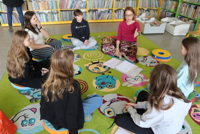 dziewczyny i kobieta prowadząca warsztaty siedzą na kolorowym dywanie