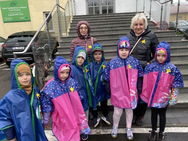 przedszkolaki i dwie osoby dorosłę pozują do zdjęcia przed schodami do urzędu, do kurtek mają przypięte żółte żonkile z papieru