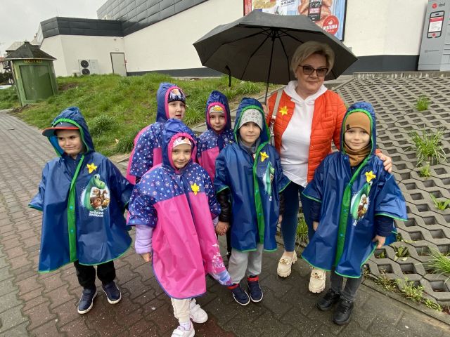 przedszkolaki i kobieta z parasolem pozują do zdjęcia, do kurtek mają przypięte żółte żonkile z papieru