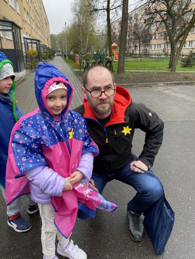 mężczyzna pozuja z dziewczynką do zdjęcia, mają do kurtek przypięte żółte żonkile z papieru