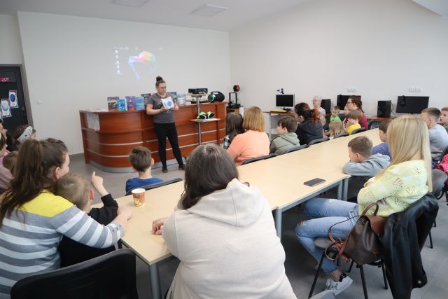 uczestnicy warsztatów siedzą przy stolikach i słuchają opowieści o kosmosie kobiety, sala komputerowa