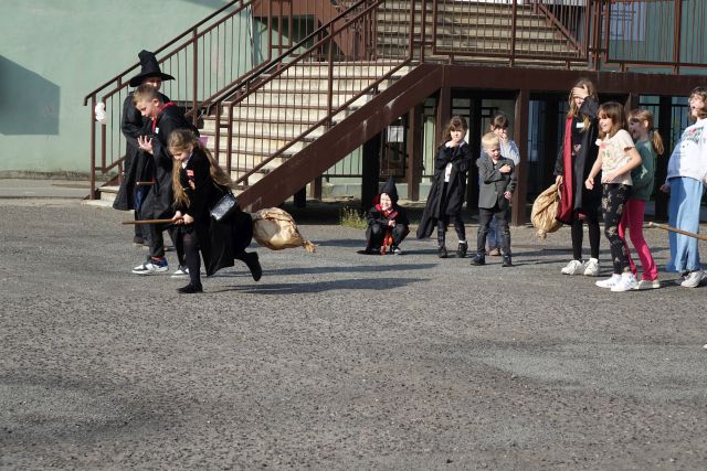 uczesnicy dnia harego pottera biorą udział w wyścigach na miotłąch na placu przed budynkiem biblioteki