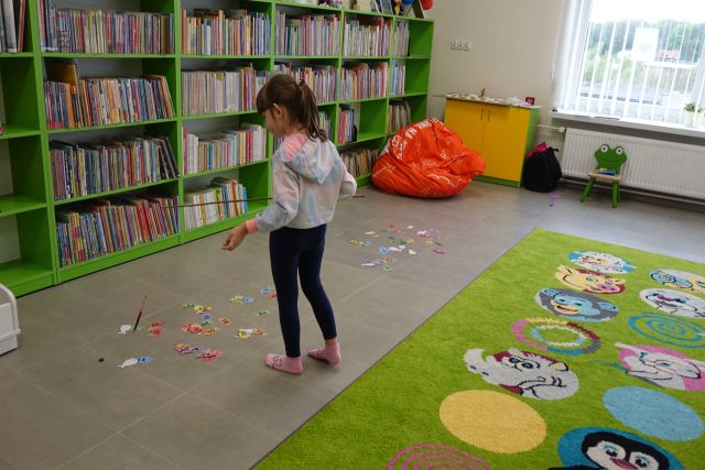 dziewczynka łowi papierowe rybki, w tle regały z książkami