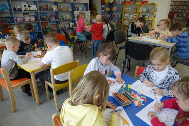 dzieci siedzące przy stolikach malują rybki