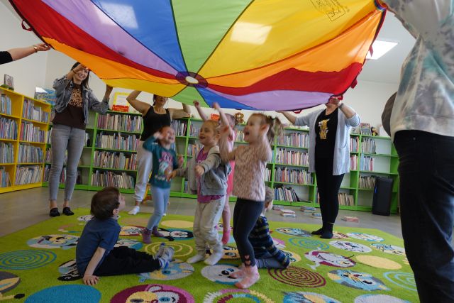 rodzice trzymają do góry kolorową chustę, pod nią dzieci