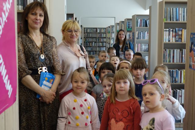 dzieci z trzema osobami dorosłymi wędrują między regałami z książkami