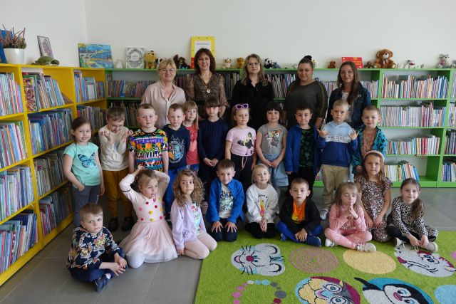 przedszkolaki z dwiema przedszkolankami i 3 bibliotekarkami pozują do zdjęcia na tle regałów z książkami