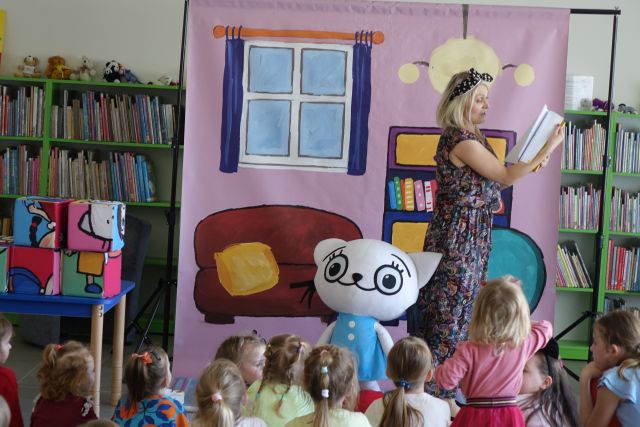 edukatorka przewraca kartki książki, obo n iej stoi duża maskotka Kici Koci