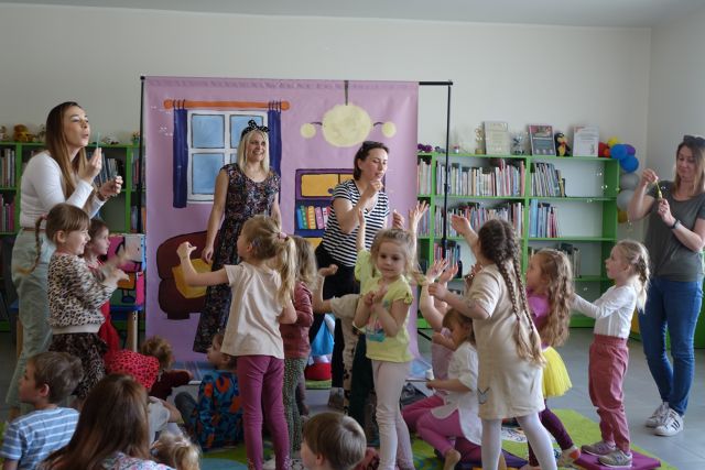 dorośli puszczają bańki mydla w kierunku dzieci siedzących na kolorowym dywanie
