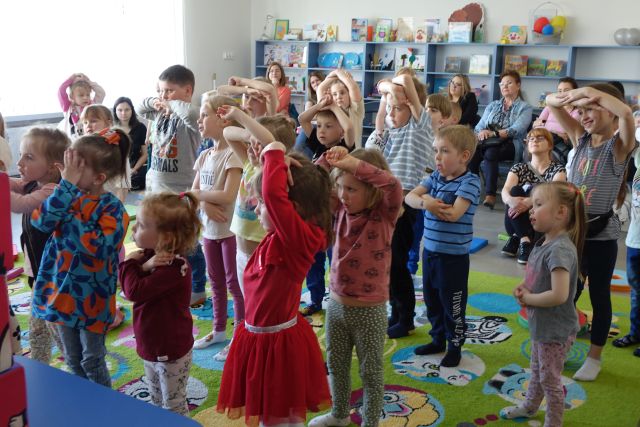 dzieci ćwiczą stojąc na kolorowym dywanie z dłońmi uniesionymi do góry