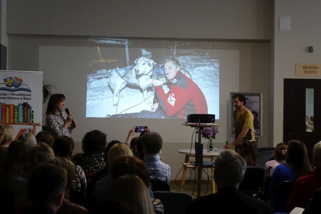 publiczność siedząca na krzesłąch słucha opowieści mężczyzny bez ręki, w tle prezentacja ze zdjęciami