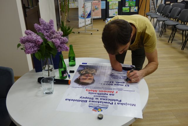 mężczyzna bez ręki podpisuje się na plakacie