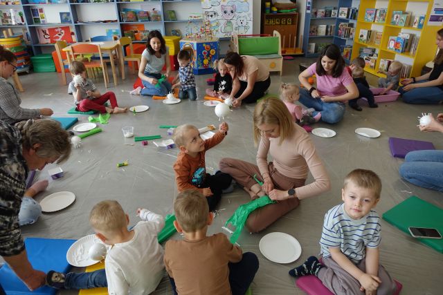 dzieci i rodzice siedzące na pufach malują styropianowe kule i zwijają folię