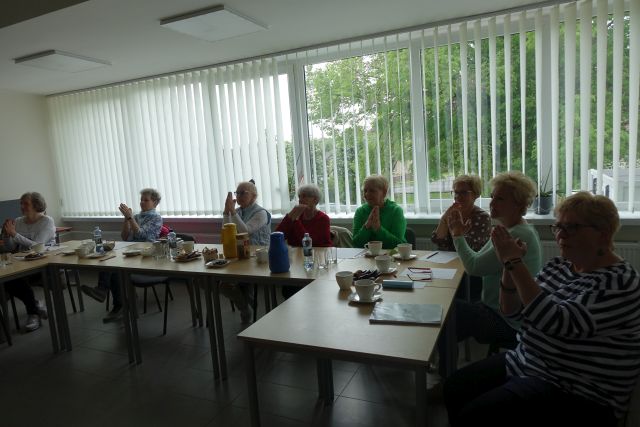 8 seniorek siedzi przy stołach