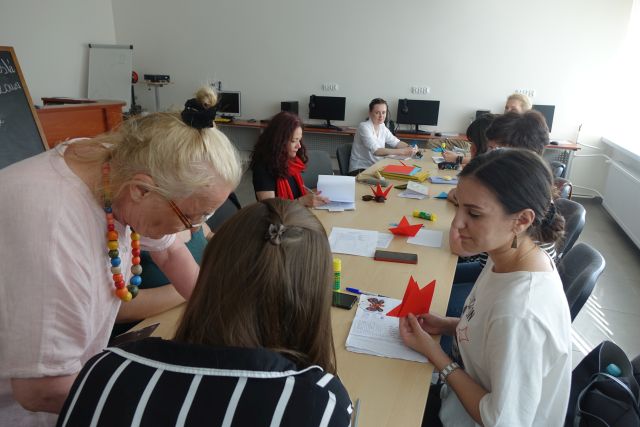 panie siedzą przy stołach i wykonują figurki origami