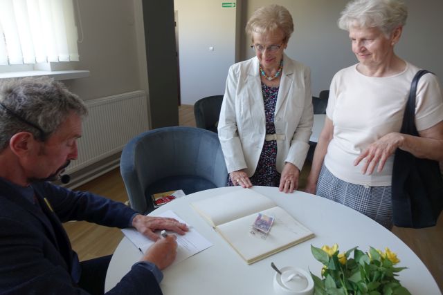 poeta podpisuje swój tomik wierszy dwóm stojącym przed nim kobietom