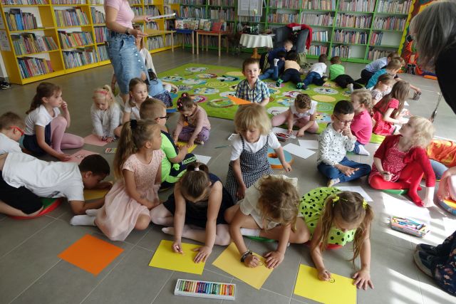 dzieci siedzą na zielonym dywanie i rysują na kartkach