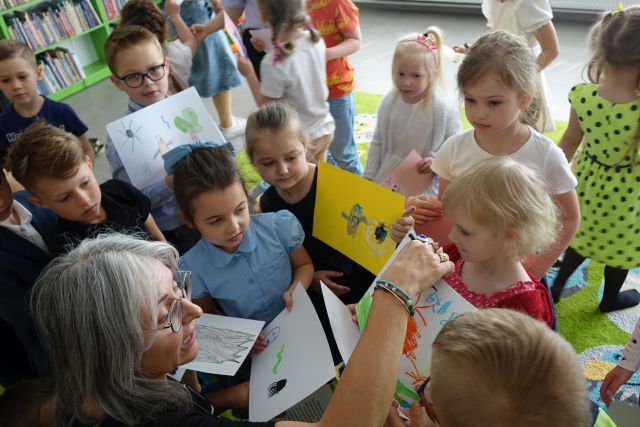 dzieci pokazują kobiecie wykonane przez siebie kdsiążeczki