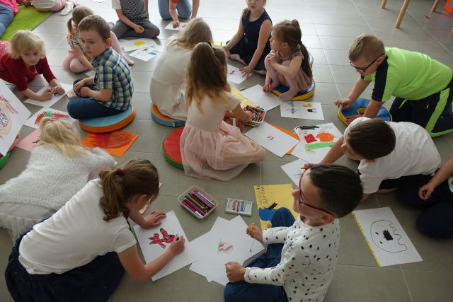 dzieci siedzą na podłodze i rysują na kartkach