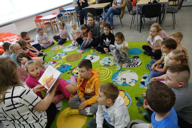 kobieta czyta dzieciom siedzącym na kolorowym dywanie